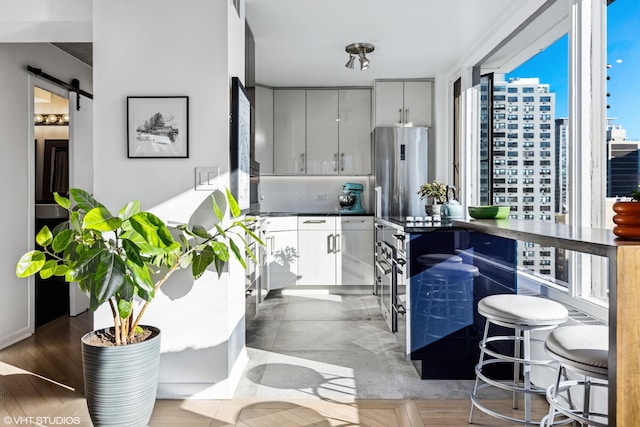 kitchen with a city view, stainless steel refrigerator, tasteful backsplash, dark countertops, and a barn door