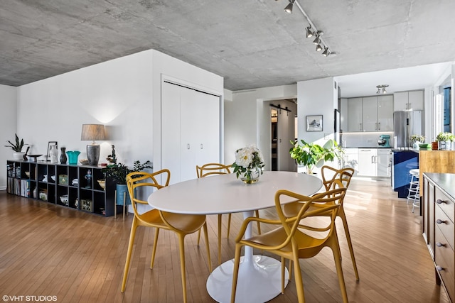 dining space with track lighting, a barn door, and light wood-type flooring