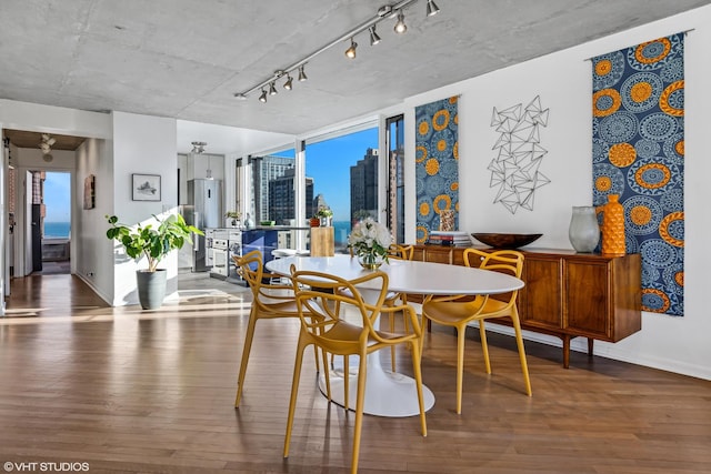 dining area with a view of city, rail lighting, wood finished floors, and baseboards