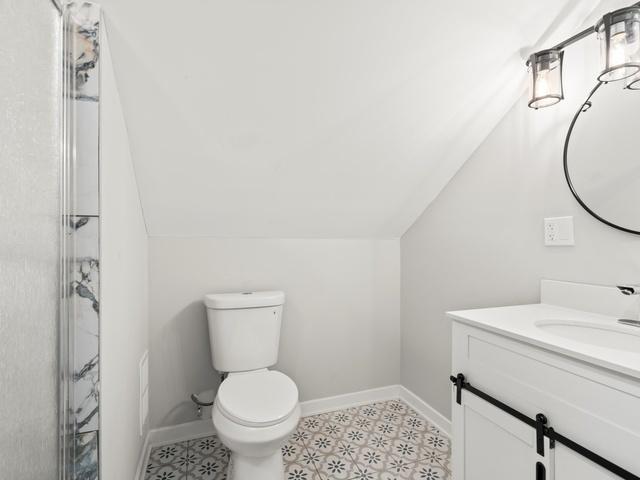 full bathroom featuring vanity, baseboards, vaulted ceiling, an enclosed shower, and toilet