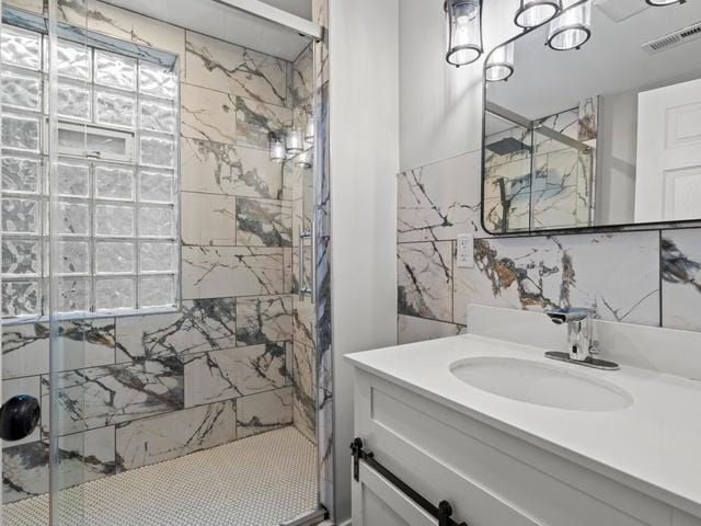 full bathroom featuring vanity, a healthy amount of sunlight, visible vents, a marble finish shower, and tile walls