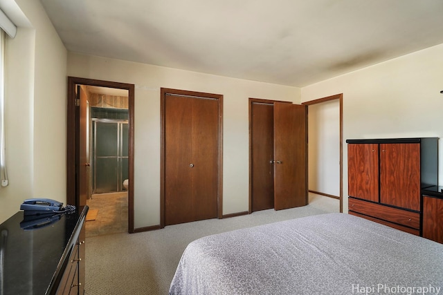 bedroom featuring light colored carpet, baseboards, and two closets