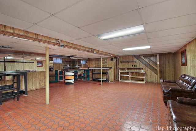 finished below grade area with tile patterned floors, a paneled ceiling, visible vents, and wood walls