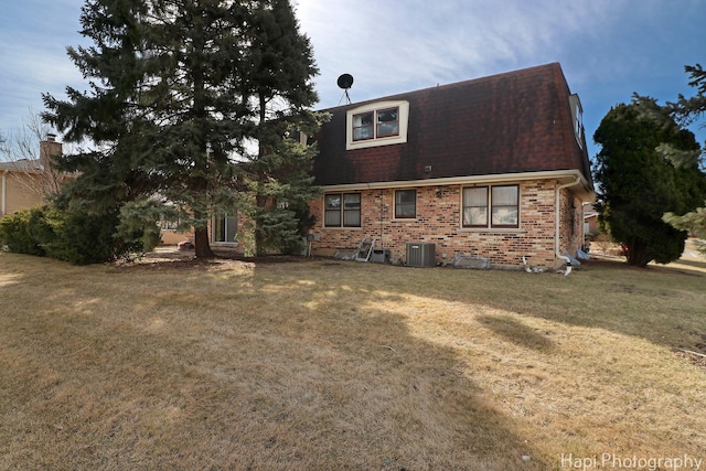 back of property featuring brick siding, central AC unit, a yard, and roof with shingles