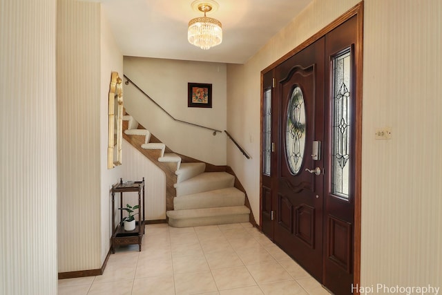 foyer entrance with stairs, an inviting chandelier, light tile patterned flooring, and baseboards