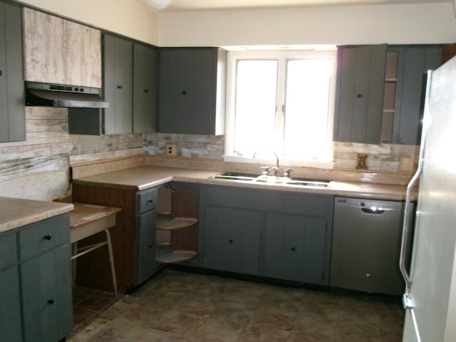 kitchen featuring freestanding refrigerator, a sink, under cabinet range hood, dishwasher, and backsplash