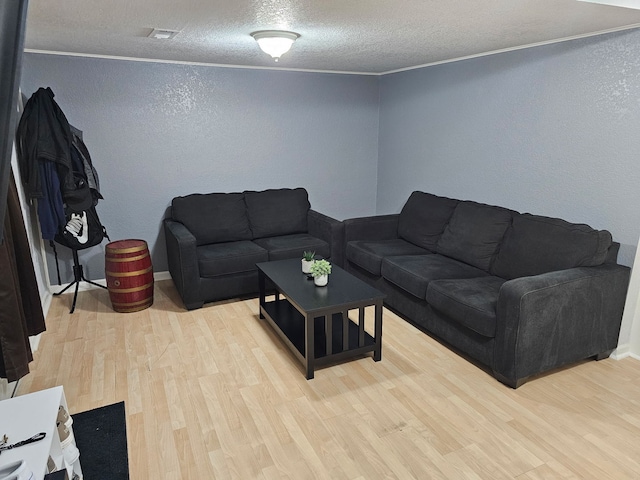 living area with a textured wall, a textured ceiling, light wood-style floors, and ornamental molding