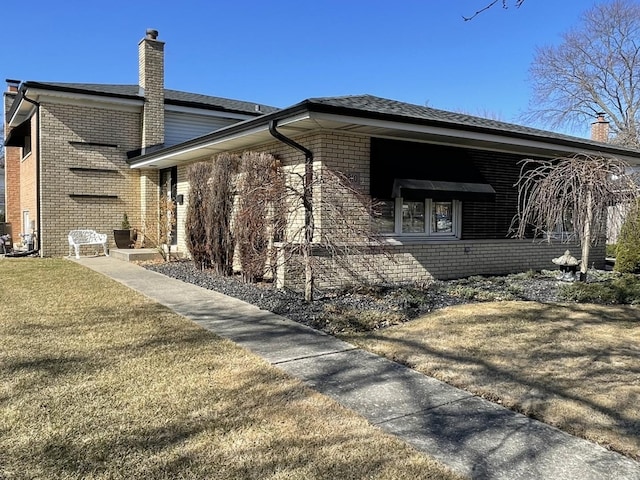 view of side of home featuring brick siding, a chimney, and a yard