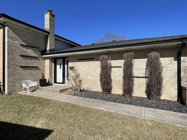 entrance to property featuring crawl space, brick siding, a yard, and a chimney