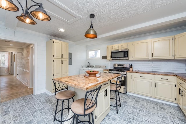 kitchen featuring a breakfast bar area, decorative backsplash, appliances with stainless steel finishes, wood counters, and washer and clothes dryer