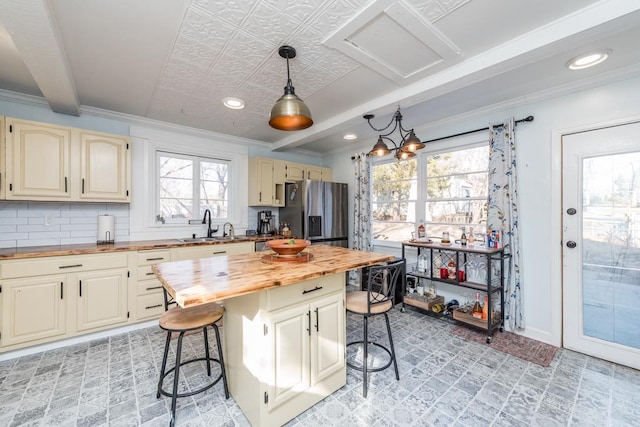 kitchen with butcher block counters, a breakfast bar, decorative backsplash, stainless steel fridge, and a sink