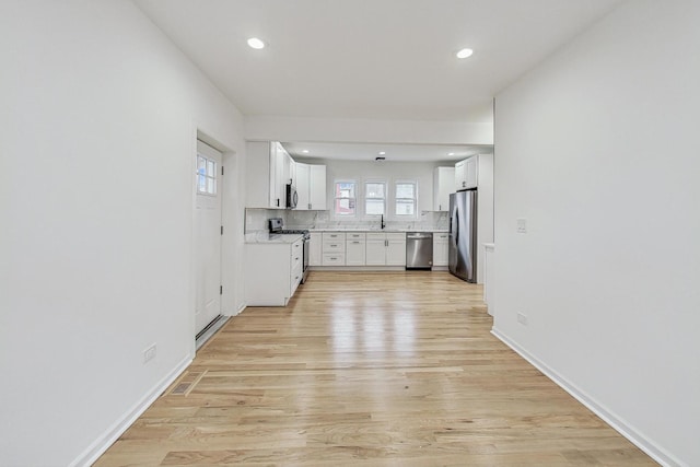 kitchen with light wood-style flooring, tasteful backsplash, white cabinetry, stainless steel appliances, and light countertops