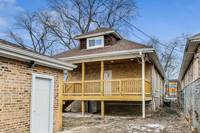 rear view of house with covered porch, brick siding, and a shingled roof