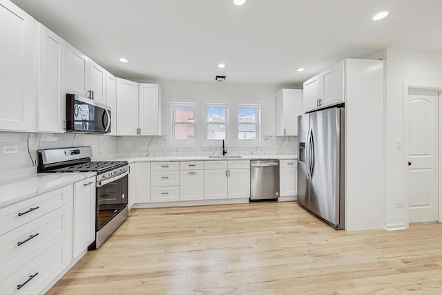 kitchen with a sink, white cabinets, appliances with stainless steel finishes, light wood-type flooring, and backsplash