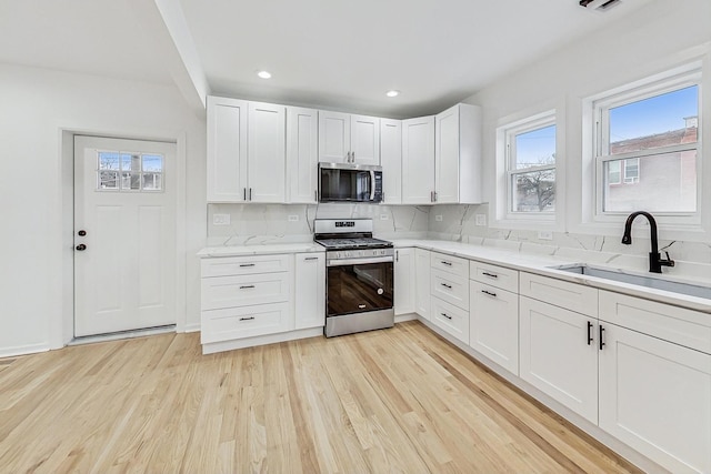 kitchen featuring a sink, backsplash, light wood-style floors, appliances with stainless steel finishes, and white cabinets