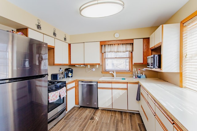 kitchen featuring wood tiled floor, a sink, stainless steel appliances, light countertops, and white cabinets