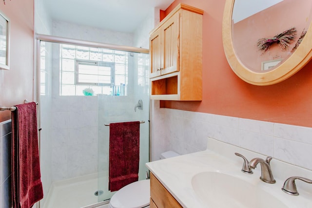 full bath with tile walls, a stall shower, toilet, and vanity