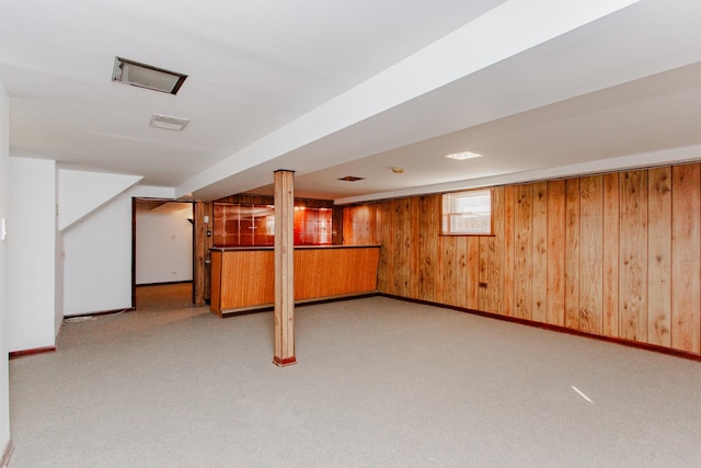 basement featuring wooden walls, carpet flooring, visible vents, and baseboards