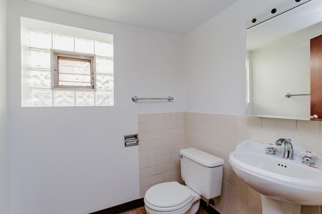 half bathroom with tile walls, toilet, a wainscoted wall, and a sink