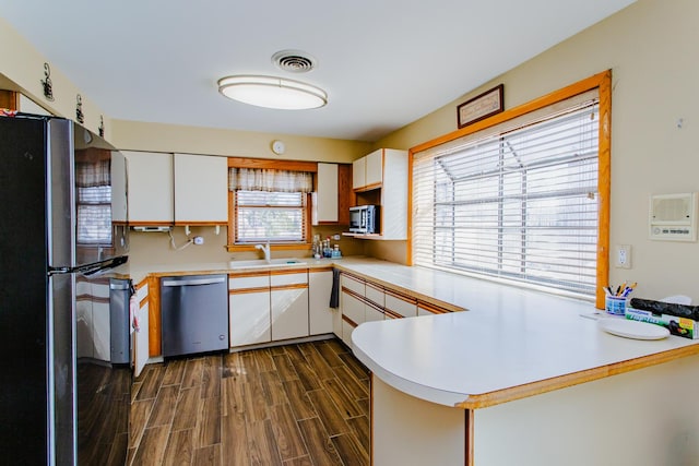 kitchen with dark wood finished floors, a peninsula, a sink, light countertops, and appliances with stainless steel finishes