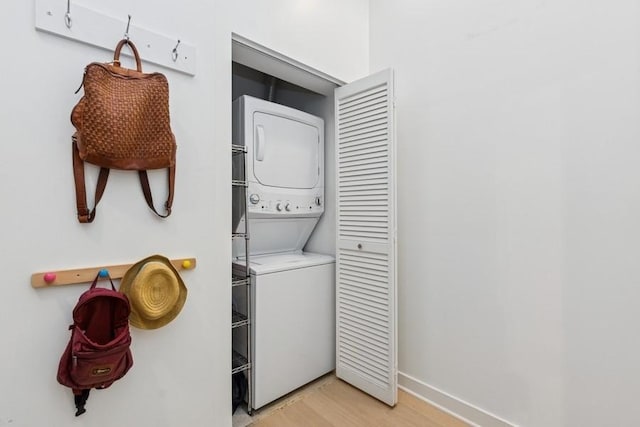 clothes washing area with laundry area, stacked washer / dryer, light wood-style floors, and baseboards