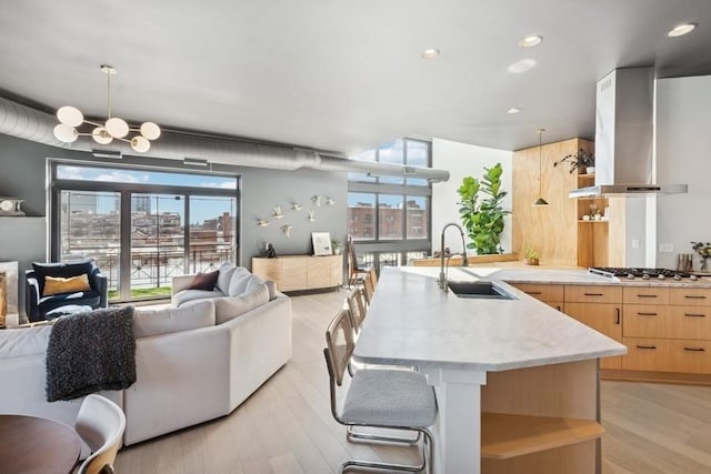 kitchen with wall chimney range hood, open floor plan, stainless steel gas stovetop, and a sink