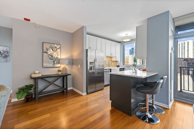 kitchen with stainless steel appliances, a peninsula, light wood-style flooring, and white cabinets