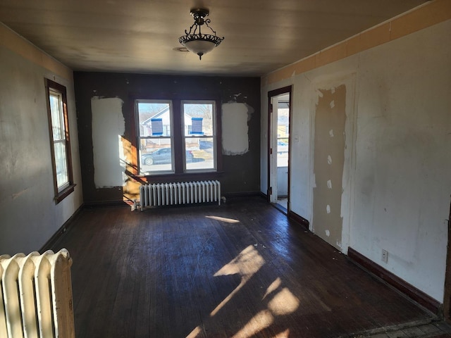 empty room featuring radiator heating unit, baseboards, and hardwood / wood-style flooring