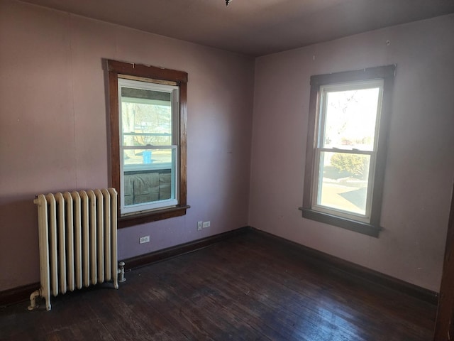 empty room featuring dark wood finished floors, radiator heating unit, baseboards, and a wealth of natural light