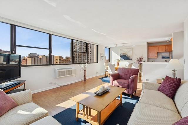 living area featuring baseboards, wood finished floors, track lighting, and a wall mounted AC