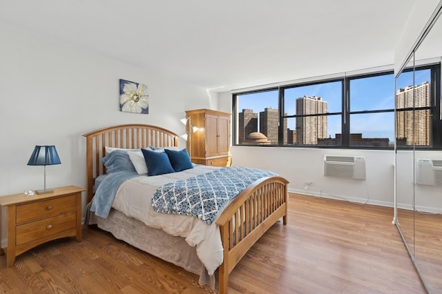 bedroom featuring a city view, a wall mounted air conditioner, baseboards, and wood finished floors