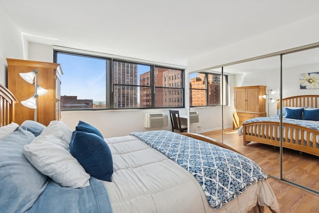 bedroom with a city view, wood finished floors, a wall unit AC, a closet, and baseboards