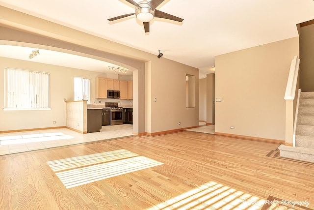 unfurnished living room with baseboards, ceiling fan, stairs, and light wood finished floors