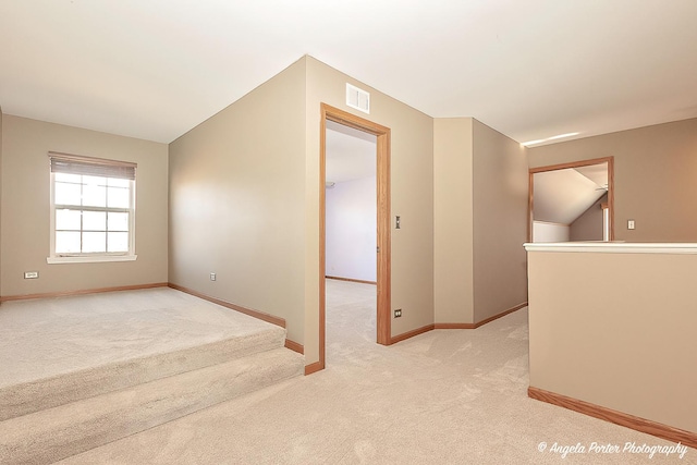 spare room featuring visible vents, light carpet, baseboards, and vaulted ceiling