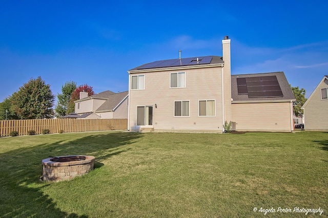 back of house featuring fence, a lawn, a chimney, and an outdoor fire pit