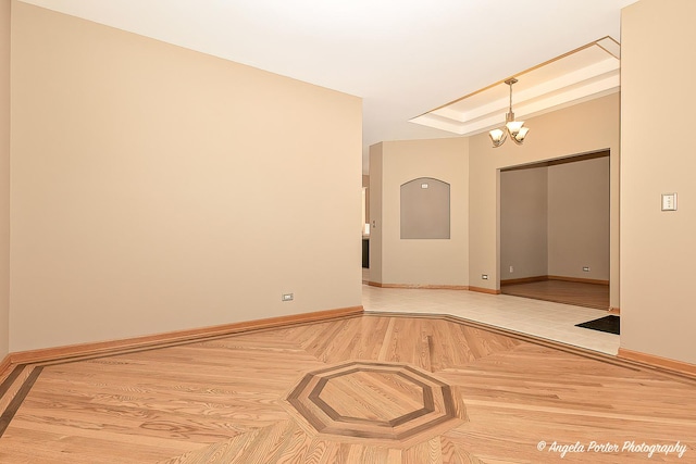 spare room featuring a notable chandelier, a raised ceiling, and baseboards