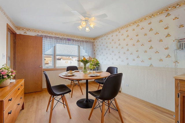 dining room featuring light wood-style floors, ceiling fan, wainscoting, and wallpapered walls