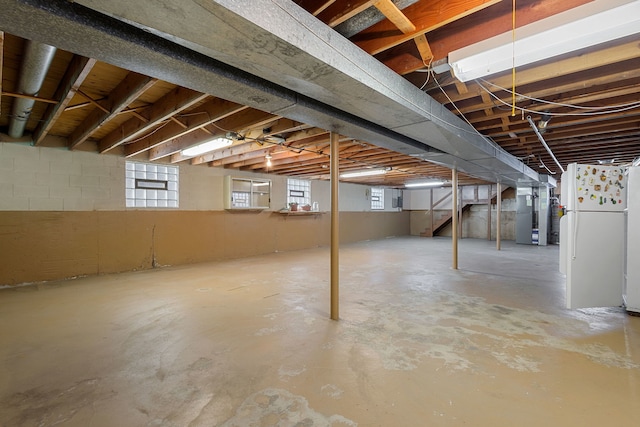 below grade area featuring concrete block wall, heating unit, and freestanding refrigerator