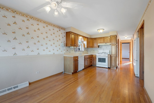 kitchen with visible vents, wallpapered walls, under cabinet range hood, a wainscoted wall, and white appliances