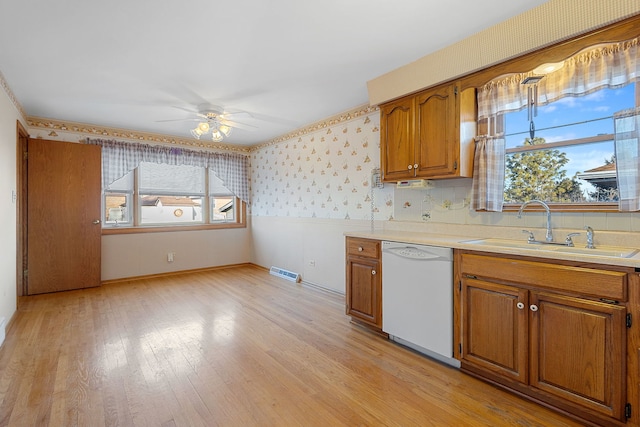 kitchen featuring wallpapered walls, ceiling fan, dishwasher, brown cabinetry, and a sink