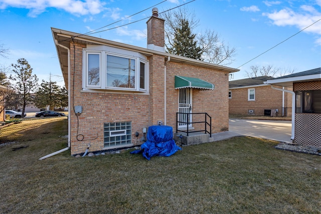 back of house with brick siding, a chimney, a lawn, and fence