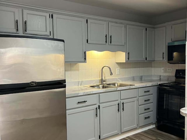 kitchen with black range with electric stovetop, a sink, freestanding refrigerator, light countertops, and decorative backsplash