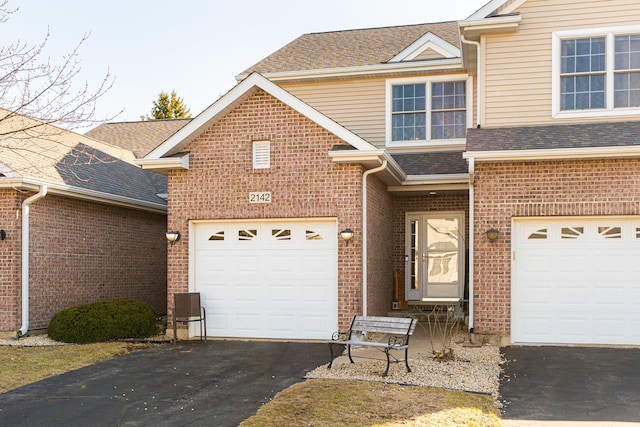 traditional-style house with aphalt driveway, a garage, a shingled roof, and brick siding