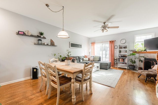 dining room featuring baseboards, a fireplace, a ceiling fan, and light wood finished floors