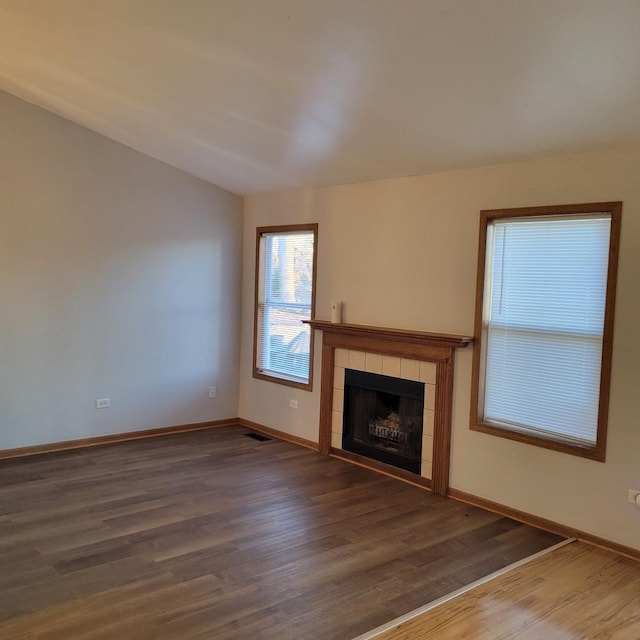 unfurnished living room with visible vents, lofted ceiling, a tiled fireplace, wood finished floors, and baseboards