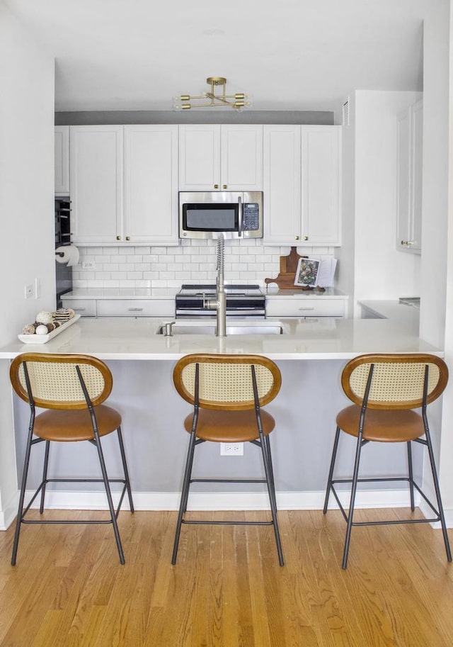 kitchen with light wood-type flooring, stainless steel appliances, tasteful backsplash, and white cabinets