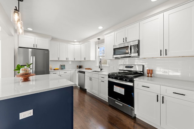 kitchen featuring a sink, dark wood-style floors, appliances with stainless steel finishes, decorative backsplash, and hanging light fixtures