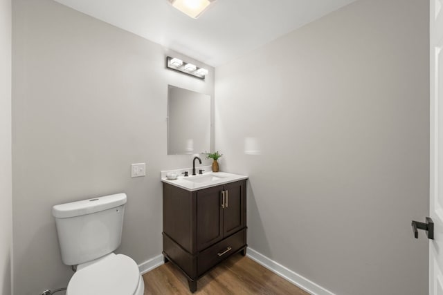 half bathroom with baseboards, toilet, wood finished floors, and vanity