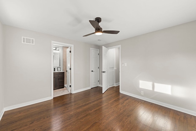 unfurnished bedroom featuring a ceiling fan, baseboards, visible vents, dark wood finished floors, and ensuite bath