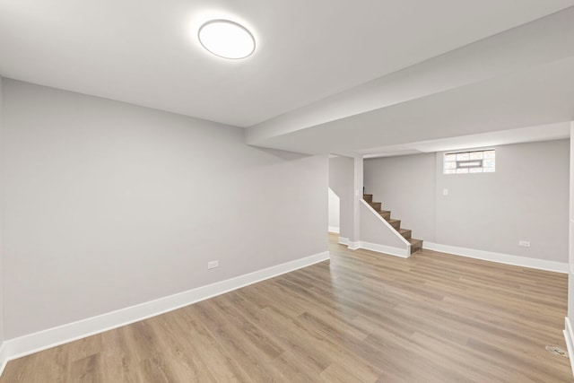 below grade area featuring baseboards, light wood-style flooring, and stairs